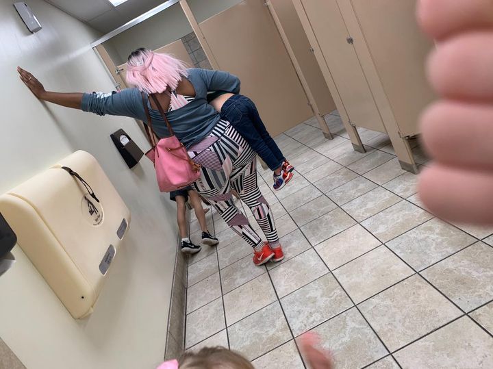 Mother leaning against a wall while holding her other child in her hand.  This in a public bathroom while her child is punished and doing push ups on the floor. 